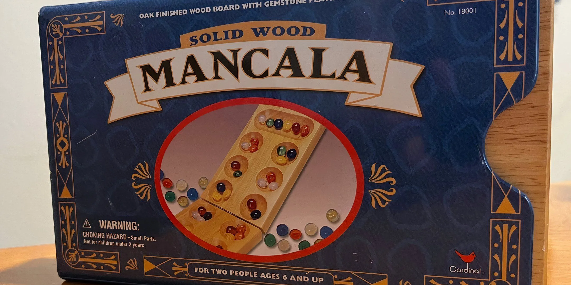 Bìa hộp game Mancala truyền thống, với những viên sỏi và hố chứa, tượng trưng cho trò chơi chiến thuật cổ xưa và đơn giản.